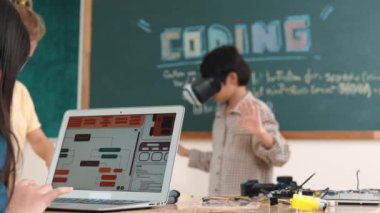 Kız kodlama sistemiyle uğraşırken metaworld 'e elektronik panoyla girmek için VR kulaklık takan bir çocuk. Çeşitli öğrencilerden oluşan bir grup program geliştirmek ve mühendislik kodu yazmak için birlikte çalışıyor. Pedagoji.