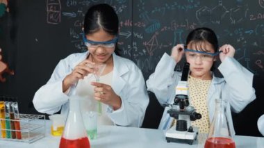 Genç lise öğrencisi deney tüpüne örnek dökerek deney yapıyor. Gözlük takan ve mikroskop altında STEM fen dersinde örnek inceleyen bir kız. Yaratıcı eğitim. Öğretim