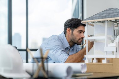 Akıllı beyaz mimar mühendisinin yakın plan portresi ev modelini incelerken aynı zamanda proje planı, proje planı ve ekipmanla birlikte mimar stüdyosunda inşaat yapmayı düşünüyor. İzleme.