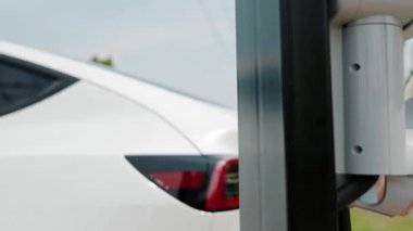 Yavaş çekimde çalışan kadın, otoparktaki EV araba aküsünü alışveriş çantasıyla şarj ediyor. Modern kadın, şehir içi seyahat tarzında çevre dostu elektrikli araçla alışverişe gider. Yararlı