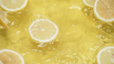 Taze limon dilimlerinin üzerine dökülen suyun sarı arkaplanı kapatın. Turunçgil meyvesinin su sıçratma ve dilimlenmiş limonla dökülme makrografisi. Tazelik. Pabulum.