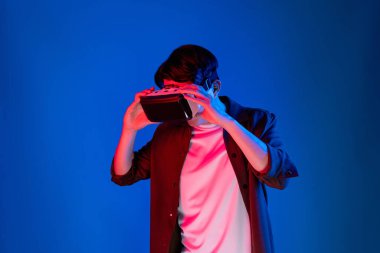 VR 'a bakan Asyalı adam, ilginç nesne teknolojisi üzerine fantastik meta-meta izlemeyi seviyor. Sanal gerçeklik üzerine mavi neon ışıklandırma arka planı. Üç boyutlu hologram yeniliğinde yeni dünya. Entrika.