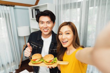 Gülümseyen sunucu şefler akıllı telefonlarıyla fotoğraf çekiyorlar. Özçekim yoluyla. Yemek programında çift hamburger tutuyorlar. İnfobahn.