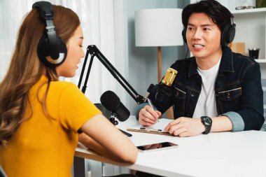 Gülümseyen radyo etkili sunucusu kulaklık takıyor kadın konuşmacı ile röportaj yapıyor sosyal medya internet sitesinden dinleyicilere bilgi paylaşıyor stüdyo kaydında sabah canlı yayın kanalı. İnfobahn.