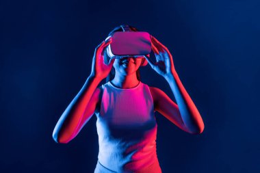 Siberpunk neon ışıklı cihazlarla çevrili zeki bir kadın metaevrene bağlı VR kulaklık takıyor, gelecekçi siber uzay teknolojisi. Zarif bir kadın sanal ortamda yaratılmış gibi görünür. Halüsinasyon.