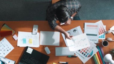 Akıllı tasarımcının renkli paletlerden renk seçmesine yardım ederken yukarıdan aşağı görünümü. Dizüstü bilgisayardan logoya bakarken birlikte çalışan ve planlayan iş adamlarının hava görüntüsü. Sempozyum.