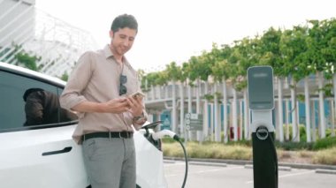 Genç adam, EV şarj aletini şehrin alışveriş merkezinin otoparkındaki şarj istasyonundan elektrik aküsünü şarj etmek için kullandı. Sürdürülebilir şehirde EV aracı tarafından şarj edilebilir enerji olarak kullanıldı.