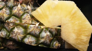 Taze ananaslı ve ayrı siyah arkaplanlı bir ananas dilimli videoyu kapat. Kaba ve balmumu kabuğu, dikenli yeşil yapraklardan bir taç, yemek fotoğrafçılığı. Geliştirilebilir.