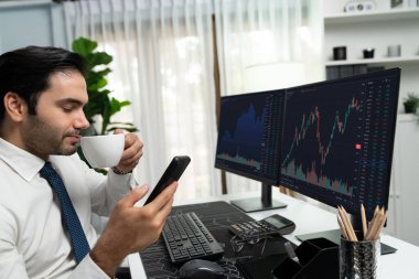 Elinde telefon dinamiğine odaklanan kahve fincanı tutan borsa yatırım ekranı veri analizini karşılaştırarak iç işlerinde yüksek kârlı finans teknolojisi pazarına yatırım yapıyor. Tahmin et..