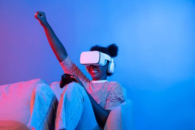 3D hologram ekranında VR kontrol çubuğu takan gülümseyen Afrikalı Amerikalı oyuncu dijital fütüristik teknoloji metaevren dünyasını birbirine bağlayan izole edilmiş neon ışığı kullanıyor. Entrika.