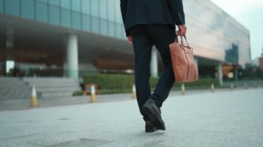 Çantayı tutarken yürüyen yetenekli iş adamının yakın çekimi. Proje yöneticisinin bacağa odaklanmış görüntüsü. Seyahat, taşınma, seyahat, yeni bir iş bulma, iş değiştirme. Arkadan bak. Sevinçli..