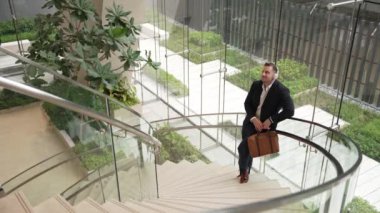 Kafkasyalı iş adamının, modern binadaki spiral merdivenlerde dikilirken kulaklık takıp rahatlatıcı müzik dinlemesinin en üst görüntüsü. Proje yöneticisi kafiyeye geçerken şarkıyı dinlemeyi sever. Urbane.