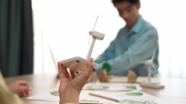 İş kadını temiz enerjiyle temsil edilen yel değirmeni modelini tutuyor. Tahta blok sembolize ekoloji evi ve yeşil güç grafiği masanın üzerinde dağılıyor, iş adamı dizüstü bilgisayarla çalışıyor. Tanımlama.