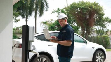 Evde EV şarj istasyonu kurulumu üzerinde çalışan nitelikli teknisyen, EV için dizüstü bilgisayarla şarj sisteminde sorun çıkarma ve yapılandırma ayarları yapıyor. Titiz