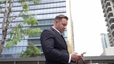 Şehir merkezindeki telefona bakan iş adamının düşük açılı kamera görüntüsü. Beyaz yöneticiler iyi haberler alırken aynı zamanda akıllı telefonlardan başlangıç projesindeki yatırımları ya da terfi almayı kontrol ediyorlar. Urbane.
