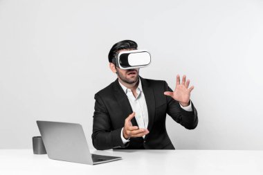 Profesyonel proje yöneticisi dizüstü bilgisayar başında otururken VR gözlüğü kullanıyor. Görsel gerçeklik kulaklığı takan yetenekli bir iş adamı metaevren ya da görsel dünyayı birbirine bağlıyor. Yenilik. Sapma.