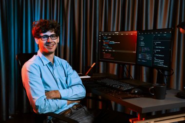 Ekranda yazılım geliştirme bilgisine karşı oturan gülümseyen bilişim geliştiricisinin profili, web sitesindeki son sürüm uygulaması için program kodlaması oluşturarak çevrili kameraya bakıyor. Toplayıcı.