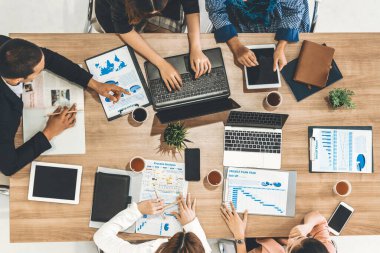 Modern ofisteki iş adamları ve iş kadınlarıyla grup toplantısındaki iş adamlarının en üst düzey görüşü, masada dizüstü bilgisayar, kahve ve belge ile. Kurumsal şirketler uds