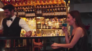 Gülümseyen güzel bir kadın konuğun yanında canlı bir şekilde zeki bir barmenle oturup cuma günkü kulüpte lüks tezgah barında mavi Hawaii kokteyli ve viski içerken. Vinosity.