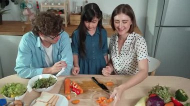 Çekici beyaz anne ve baba Asyalı kızıyla taze yemek pişirmek için birlikte vakit geçiriyorlar. Enerjik anne ve baba mutfakta salata yapmak için taze sebze hazırlıyor. Sağlıklı yiyecekler. Pedagoji.