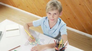 Yaratıcı resim boyayan ve sanat dersinde okuyan mutlu çocuk. Sevimli beyaz çocuk çevrimiçi test yaratıcı öğrenme eğitiminde renklendirme kitabı öğrenmekten zevk alıyor ya da heyecan duyuyor. Üst Manzara. Etkinlik.