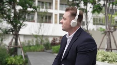 Profesyonel iş adamı kulaklık takıyor ve yeşil şehirde rahatlatıcı müziğe geçiyor. Kafkasyalı proje yöneticisi, Eko Kent 'te oturup dinlenirken şarkı eşliğinde dans ediyor. Yaşam tarzı. Urbane.