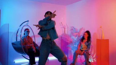 Çok kültürlü bir arkadaş kürsüde otururken Asyalı yetenekli bir dansçı modern müziğe geçiyor. Profesyonel dansçı, hipster takımı tezahürat yaparken ve desteklerken enerjik adımlar atıyor. Mutluluk.