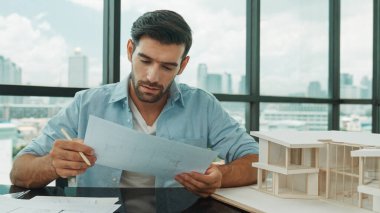 Planı elinde tutarken evin modelini kontrol eden zeki mühendisin portresi. Profesyonel iş adamı proje seçerken mimarın modeline bakar ve tasarım yapmayı düşünür, seçer. Tartışma