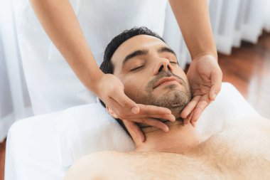 Beyaz adam stres önleyici kafa masajından ve lüks bir tatil beldesi veya otel spa salonundaki modern ışık ortamında yüz güzelliği eğlencelerini şımartmaktan hoşlanıyor. Sessiz.