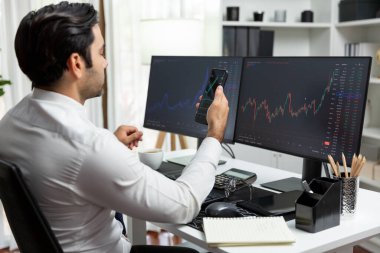 Akıllı telefondan akıllı telefon arayan tüccar işadamı, bilgisayardaki dinamik borsa yatırım ekranını analiz ediyor ve modern merkez ofisteki en kârlı finansal teknoloji pazarına yatırım yapıyor. Tahmin et..