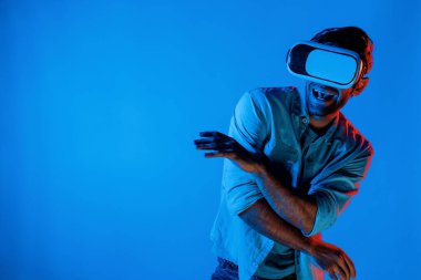 Yakışıklı, dans eden ve müziğe hareket eden bir adam. VR gözlüğü ve neon ışıklı arka plan kullanarak. Beyaz erkek oyuncu, teknolojik yenilikler giyerek pop müzik dinlerken ayakta duruyor. Sapma.