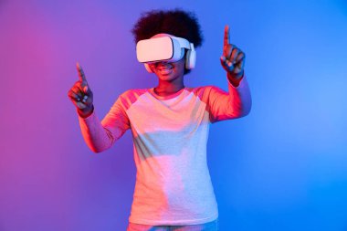 Genç Afrikalı, mavi pembe neon aydınlatma grafikli dijital yenilik 3 boyutlu hologram gramında veri öğrenme uygulaması ile metaevren boyunca VR gözlük takıyor. Entrika.