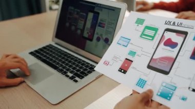 Mobil uygulama için kullanıcı arayüzü prototipini ofis çalışanlarına sunan harika bir şirket çalışanı. UX UI tasarımcısı kağıt üzerinde simge tasarımının işlevini açıklıyor. Sinerjik