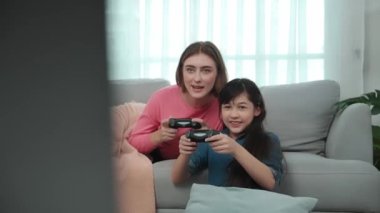 Annem kanepede yatarken, mutlu kız oyun oynuyor ve oturuyor. Beyaz bir ebeveyn ve çekici zeki bir kız elinde joystick ile birlikte vakit geçirip maç kazanmaya odaklanıyor. Yaşam tarzı. Pedagoji.