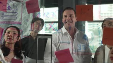 Cam duvarda yaratıcı fikirleri paylaşmak için renkli yapışkan notlar kullanarak pazarlama fikrini değerlendiren mutlu profesyonel iş adamları. Bir grup farklı iş adamları strateji hakkında tartışıyorlar. Yönlendirici.