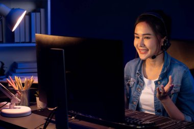 Sunucu kanalı Asyalı etkileyicisi canlı yayında konuşuyor. Sosyal medyada kulaklık takıyor, bilgisayar kaydı yapıyor, dinleyicileri selamlıyor ve Neon Modern Stüdyoları 'nda online olarak koçluk yapıyor. Taktik.