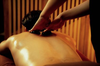Sıcak mum ışığıyla lüks bir tatil köyündeki kaplıca salonunda sıcak taş masajı, mutlu erkek müşteri bazalt taşı masajının keyfini çıkarırken rahatlatıcı bir sıcaklıkla vücudun üzerinde süzülüyor. Sessiz.