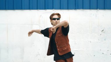 Beyaz arka planda break dans pratiği yapan yakışıklı bir sokak dansçısı. Hip hop tarzı giyinen sporcu, mavi arka planlı bir sokakta müzik eşliğinde ayak sesleri çıkarıyor. Açık hava sporu 2024 hiphop..
