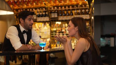 Gülümseyen güzel bir kadın konuğun yanında canlı bir şekilde zeki bir barmenle oturup cuma günkü kulüpte lüks tezgah barında mavi Hawaii kokteyli ve viski içerken. Vinosity.