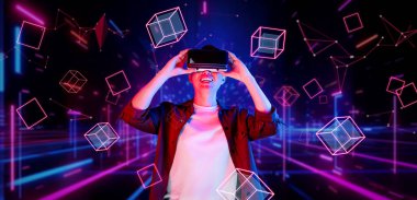 Afrikalı adam, VR kulaklık takıp parlak mavi ve pembe geometrik şekillerde dururken metaevreni keşfetmek için heyecanlanıyor. Oyuncu artırılmış gerçeklik gözlüğü kullanırken oyun oynuyor. Yaratıcılık.