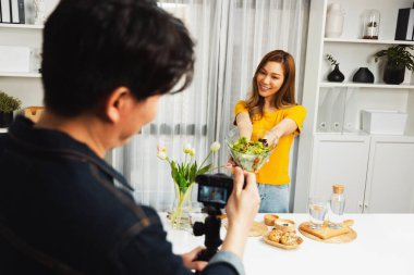 Asyalı güzel kadın yemek uzmanı blog yazarı akıllı kameramanın sosyal medya kavramında canlı yayında kaydettiği canlı yayında salatanın nasıl kolay pişirileceğini öğretiyor. İnfobahn.