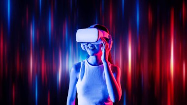 Zeki bir kadın, metaevreni birbirine bağlayan VR kulaklık takan neon ışıklarla çevrili duruyor. Gelecekteki siber uzay topluluğu teknolojisi. Uzaklara bakan zarif bir kadın ve tatmin edici bir şekilde gülümsüyor. Halüsinasyon.