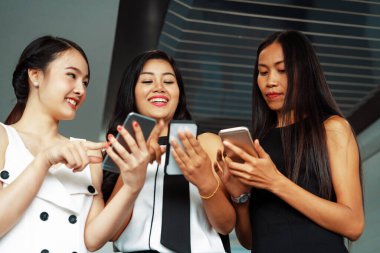Üç kadın arkadaş ellerinde cep telefonuyla sohbet ediyorlar. Sosyal medya, dedikodu haberleri ve online alışveriş kavramı. uds