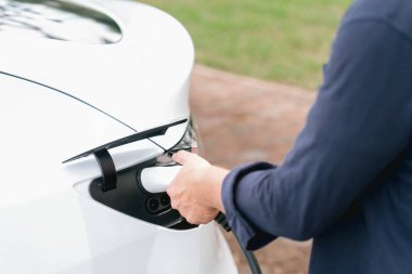 Açık yeşil şehir parkı manzaralı EV şarj istasyonundan EV elektrikli araçları şarj eden adam. Çevre dostu şehir ulaşımı ve çevre dostu EV araba seyahati. Yükselt