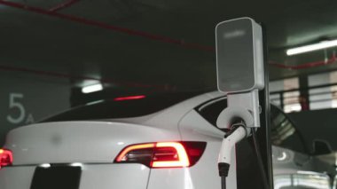 Şehir merkezindeki kapalı otoparkta yavaş çekimde EV elektrikli araba şarj oluyor. Şehir merkezinde sürdürülebilirlik yeşili, yeniden şarj edilebilir elektrikli araç iç organları.