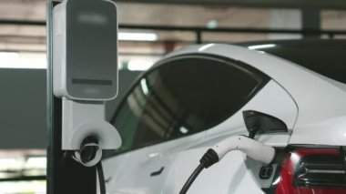 Şehir merkezindeki kapalı otoparkta yavaş çekimde EV elektrikli araba şarj oluyor. Şehir merkezinde sürdürülebilirlik yeşili, yeniden şarj edilebilir elektrikli araç iç organları.