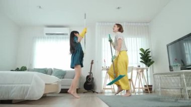 Beyaz anne ve Asyalı çocuk birlikte ev işi yapıyor ve müzik eşliğinde dans ediyorlar. Çekici anne ve kız modern yatak odasını temizlerken şarkı söyleyip rahatlatıcı müziğe atlıyorlar. Yaşam tarzı. Pedagoji.
