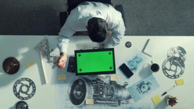 Türbin motoru veya jet motoru tasarımı ve çeşitli metal teçhizat dağılımı ile toplantı masasında yeşil ekranlı tablet üzerinde çalışırken telefona bakan mühendis görüntüsü. Hizalama.