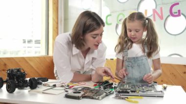 Genç, zeki, beyaz bir öğretmen öğrencilere elektronik kurulun bir parçasını öğretiyor. Uzman kız dijital elektrikli aletleri öğreniyor ve cips ve kablolarla ana kartı tamir ediyor. Etkinlik.