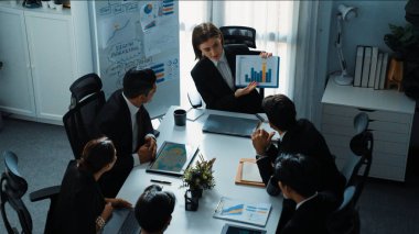 Akıllı iş kadınlarının en üst görüşü çeşitli iş adamlarına satış tablosunun arttığını gösterirken, bir grup farklı iş adamı da masada belgelerle hisse yatırım verilerini dinleyip analiz ediyor. Müdürlük.